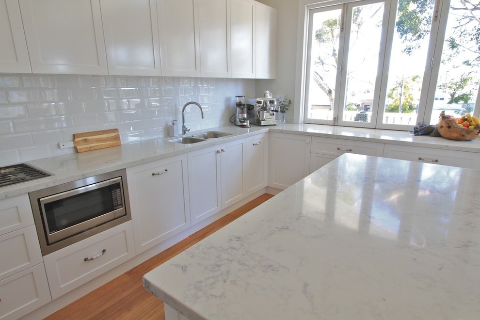 This is an example of a mid-sized beach style eat-in kitchen in Sydney with shaker cabinets, white cabinets, marble benchtops, white splashback, porcelain splashback and with island.