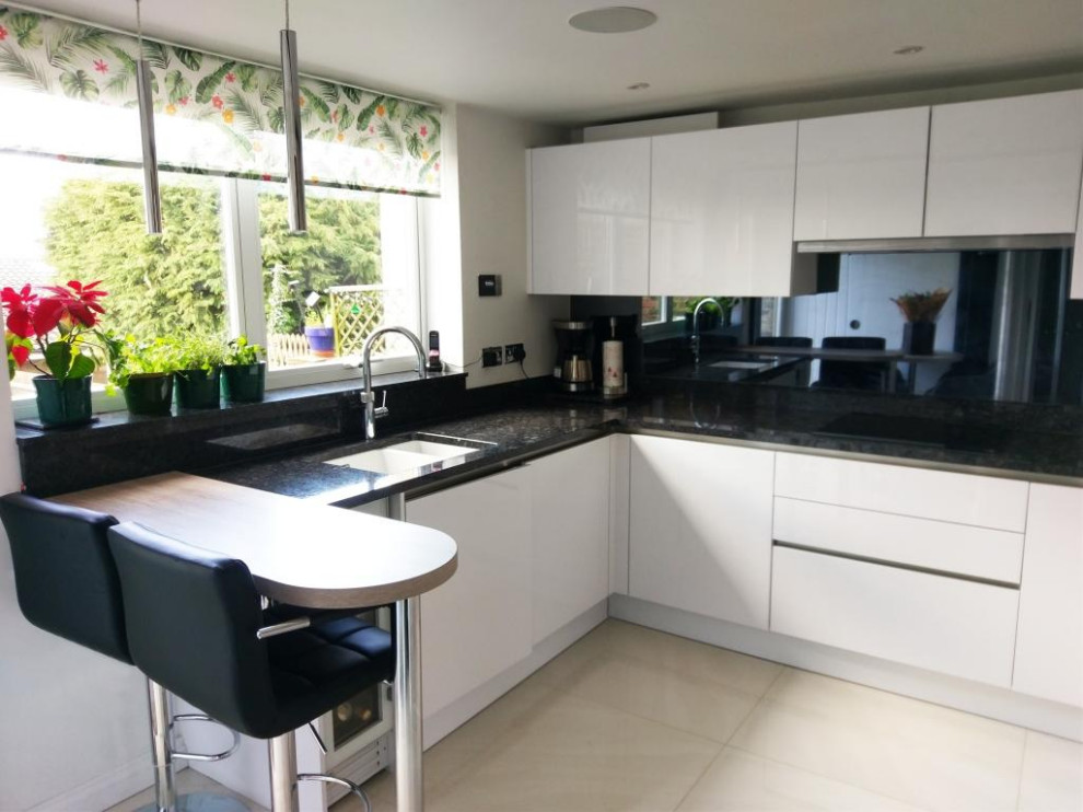 Design ideas for a small modern u-shaped eat-in kitchen in London with an integrated sink, flat-panel cabinets, granite benchtops, metallic splashback, glass sheet splashback, stainless steel appliances, ceramic floors, a peninsula, beige floor and black benchtop.