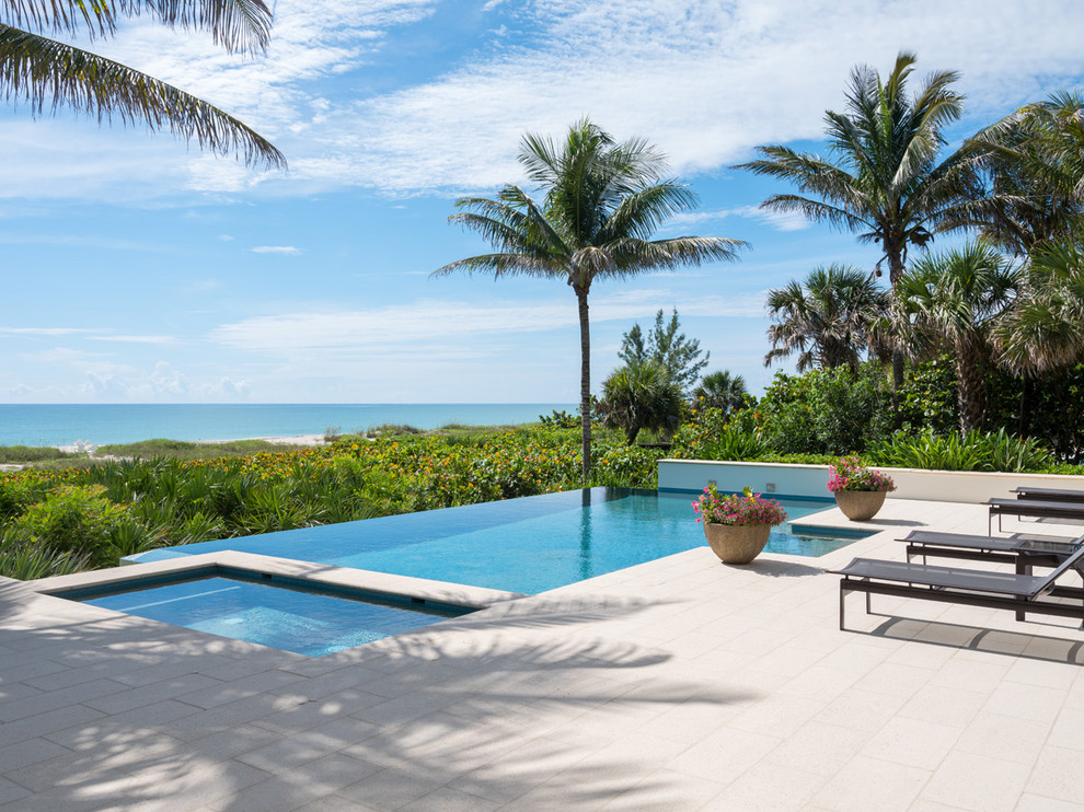 This is an example of a tropical backyard rectangular infinity pool in Other with tile.