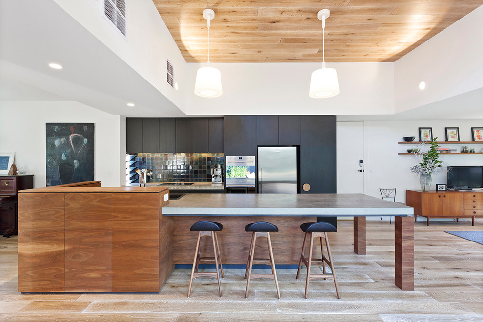 Photo of a midcentury open plan kitchen in Melbourne with flat-panel cabinets, black cabinets, concrete benchtops, stainless steel appliances, light hardwood floors, with island, beige floor and grey benchtop.