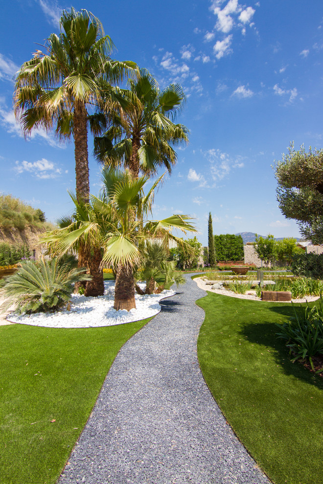 Large tropical front yard full sun garden in Barcelona with a garden path and gravel.