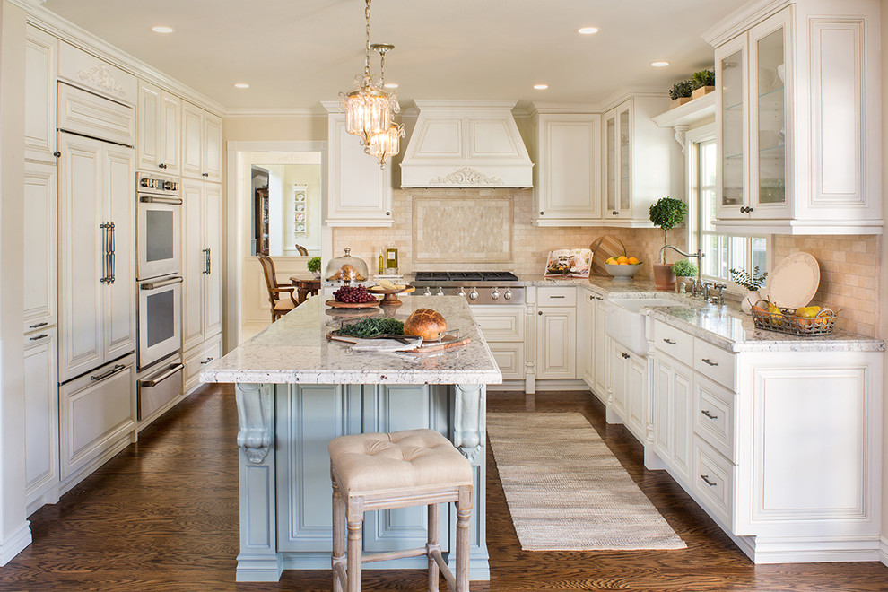 Design ideas for a traditional u-shaped kitchen in Los Angeles with a farmhouse sink, raised-panel cabinets, white cabinets, beige splashback, panelled appliances, dark hardwood floors, with island and brown floor.