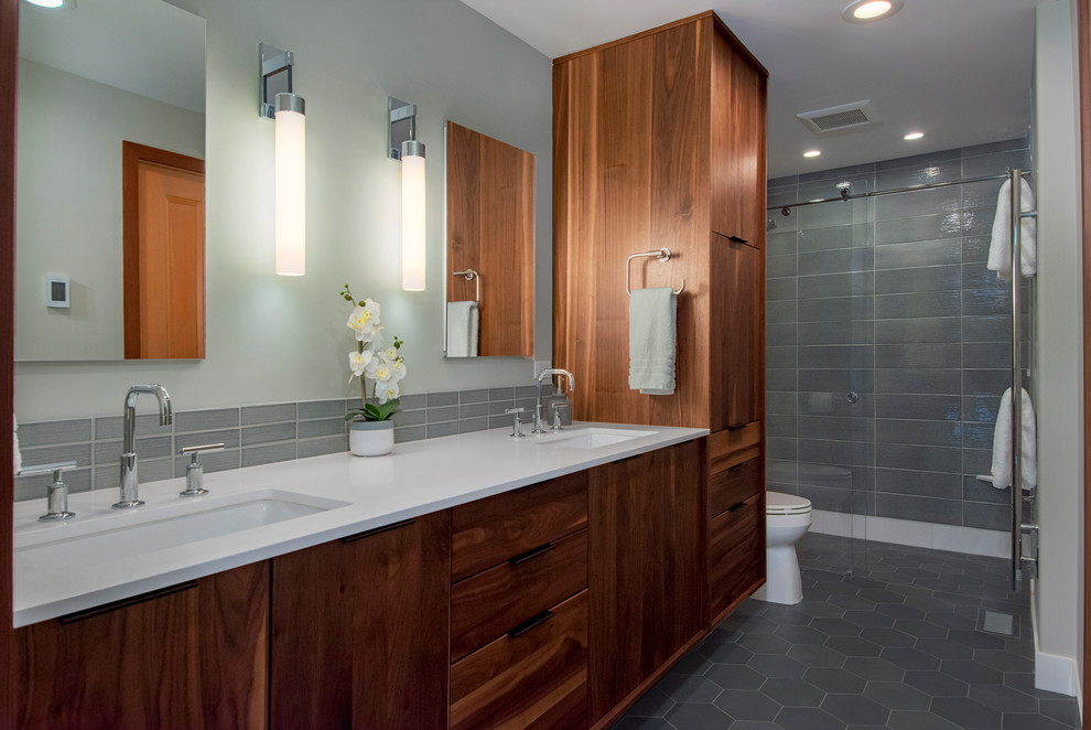 This is an example of a mid-sized midcentury master bathroom in Seattle with flat-panel cabinets, brown cabinets, a curbless shower, a two-piece toilet, ceramic tile, grey walls, porcelain floors, an undermount sink, engineered quartz benchtops, a sliding shower screen, white benchtops, gray tile and grey floor.