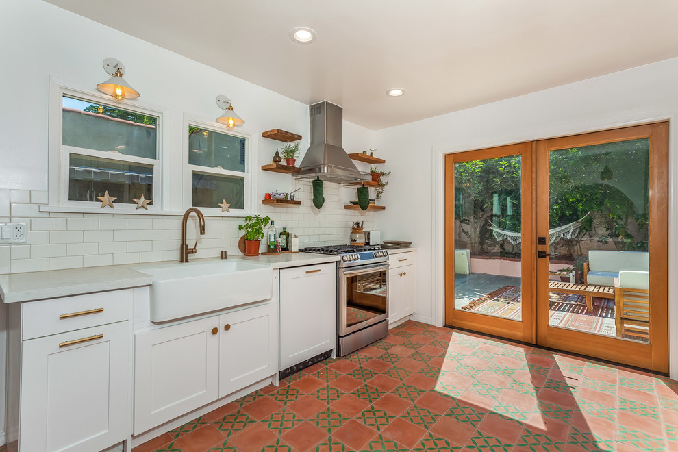 Photo of a mid-sized traditional galley separate kitchen in Los Angeles with a farmhouse sink, shaker cabinets, white cabinets, quartz benchtops, white splashback, subway tile splashback, stainless steel appliances, cement tiles, red floor and white benchtop.