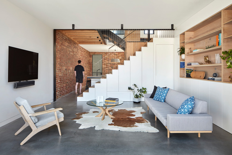 Photo of a small contemporary open concept living room in Melbourne with white walls, concrete floors, a wall-mounted tv and grey floor.