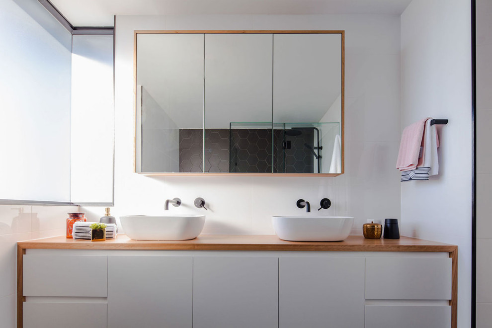 Photo of a mid-sized contemporary bathroom in Gold Coast - Tweed with flat-panel cabinets, white cabinets, a one-piece toilet, white tile, white walls, a vessel sink, wood benchtops and brown benchtops.