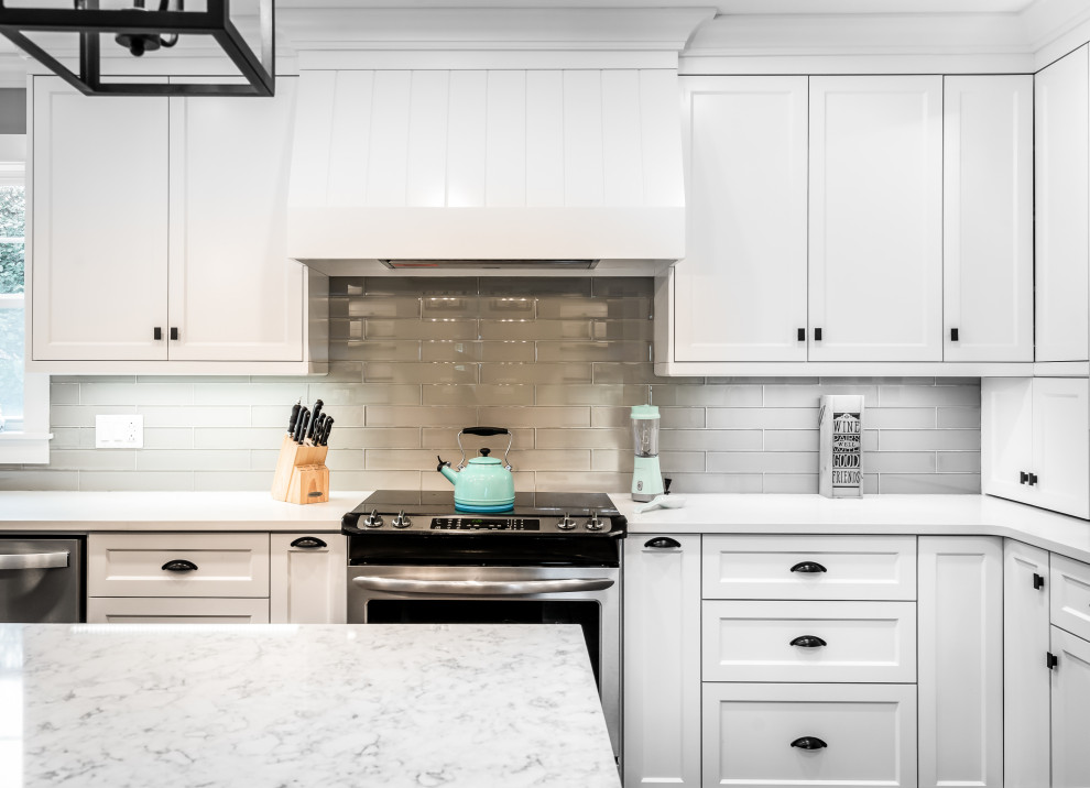 Example of a large transitional l-shaped medium tone wood floor and brown floor kitchen design with an undermount sink, white cabinets, quartz countertops, white backsplash, glass tile backsplash, stainless steel appliances, an island and white countertops