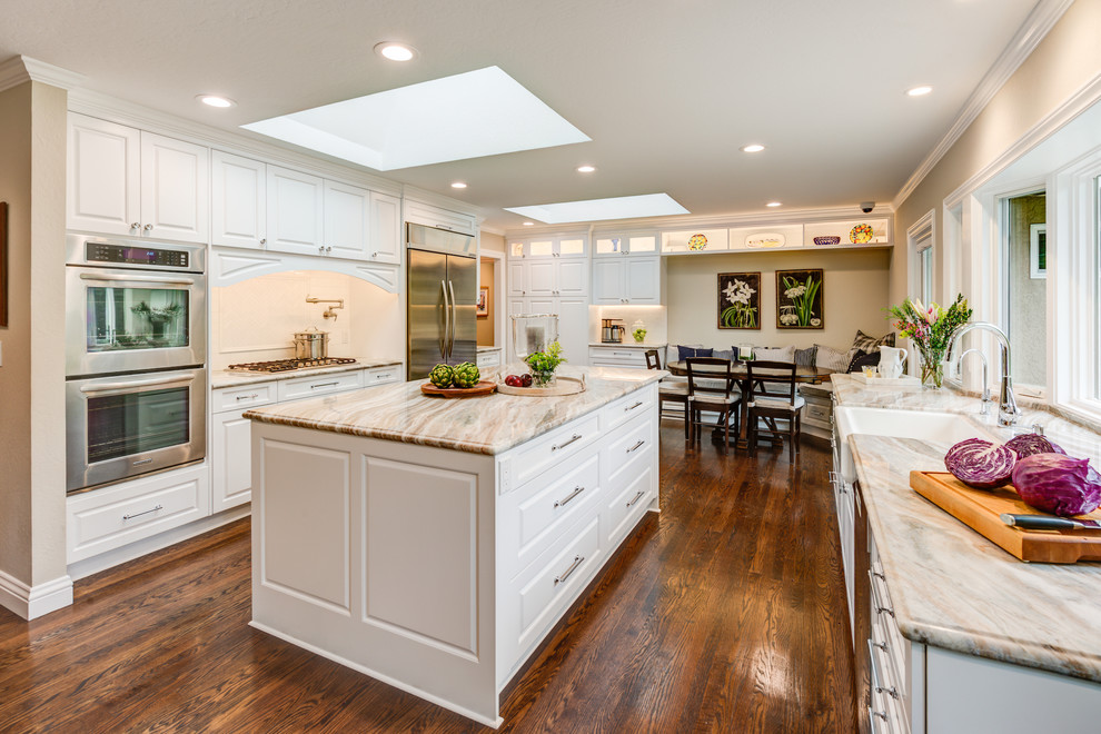 Inspiration for a large country u-shaped open plan kitchen in San Francisco with a farmhouse sink, raised-panel cabinets, white cabinets, quartz benchtops, beige splashback, subway tile splashback, stainless steel appliances, medium hardwood floors, with island and brown floor.