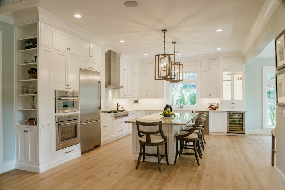 Photo of a large traditional l-shaped open plan kitchen in Charleston with a submerged sink, beaded cabinets, white cabinets, engineered stone countertops, white splashback, engineered quartz splashback, stainless steel appliances, light hardwood flooring, an island, brown floors and white worktops.