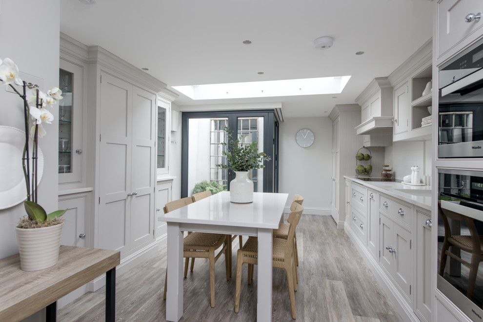Photo of a mid-sized transitional kitchen in London with a drop-in sink, shaker cabinets, grey cabinets, quartzite benchtops, white splashback, ceramic splashback, stainless steel appliances, medium hardwood floors, no island, grey floor and white benchtop.