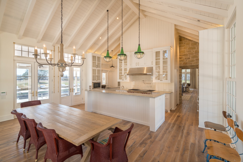 This is an example of a country u-shaped eat-in kitchen in Austin with glass-front cabinets, medium hardwood floors, with island, white cabinets, white splashback, stainless steel appliances, brown floor and grey benchtop.