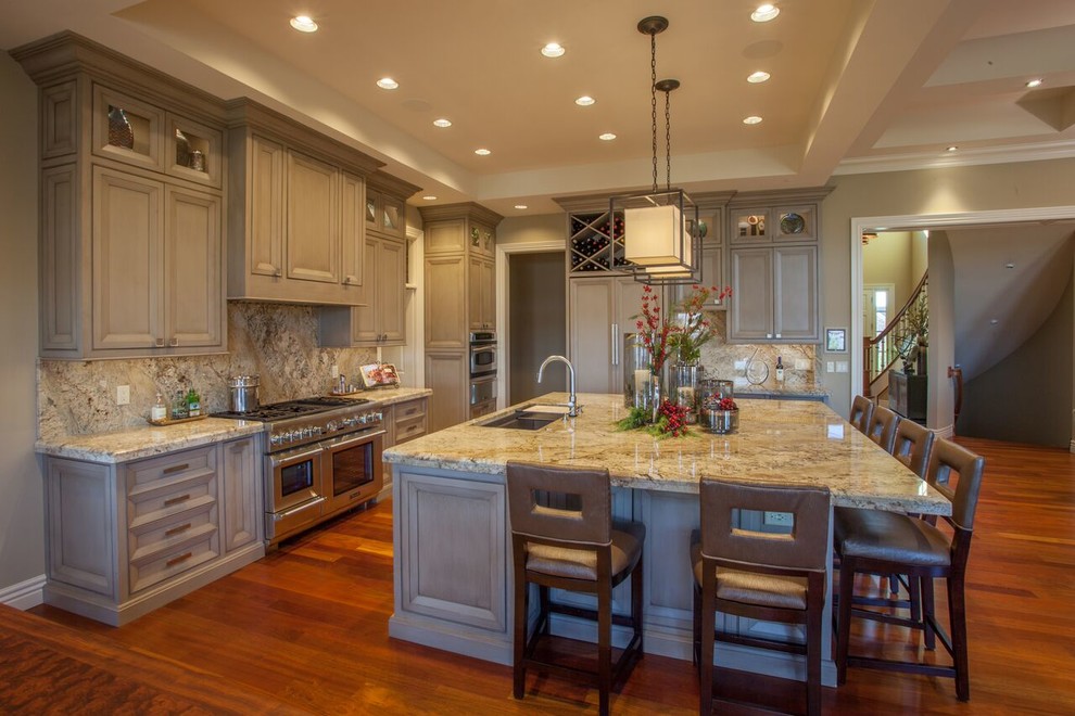 Large transitional medium tone wood floor open concept kitchen photo with recessed-panel cabinets, gray cabinets, granite countertops, beige backsplash, paneled appliances and an island
