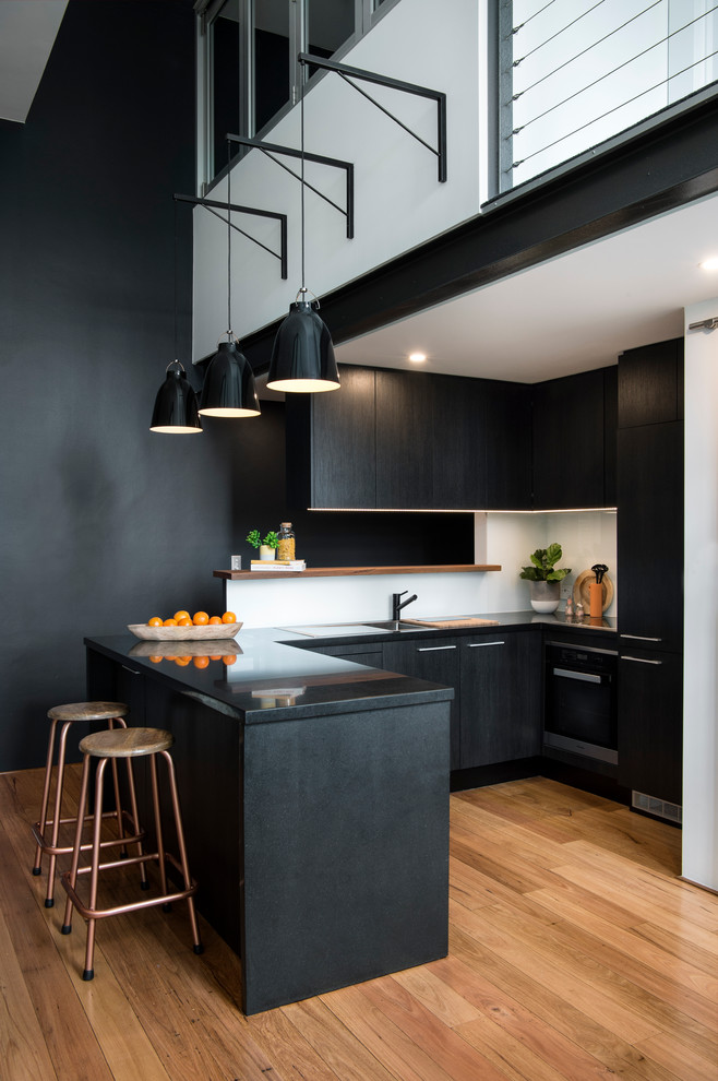 Photo of a mid-sized contemporary kitchen in Sydney with a drop-in sink, glass sheet splashback, stainless steel appliances, medium hardwood floors, flat-panel cabinets, black cabinets, white splashback and a peninsula.