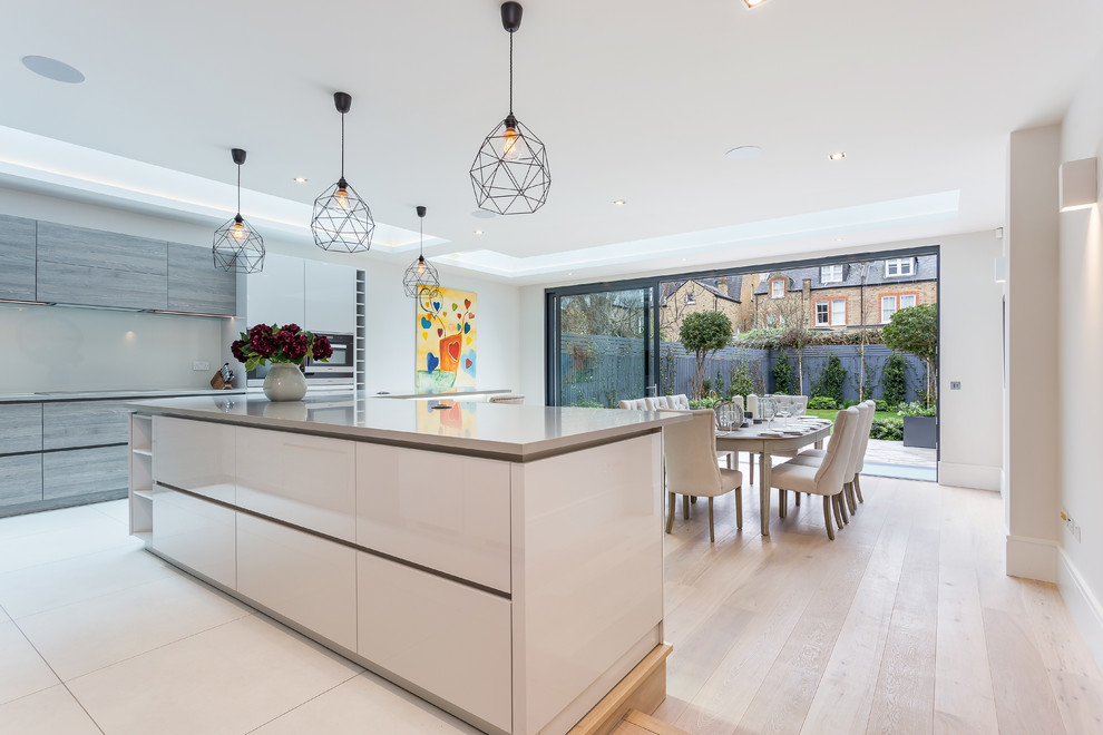 Large contemporary l-shaped eat-in kitchen in London with a drop-in sink, flat-panel cabinets, white cabinets, quartz benchtops, beige splashback, ceramic splashback, black appliances, ceramic floors, with island and white floor.