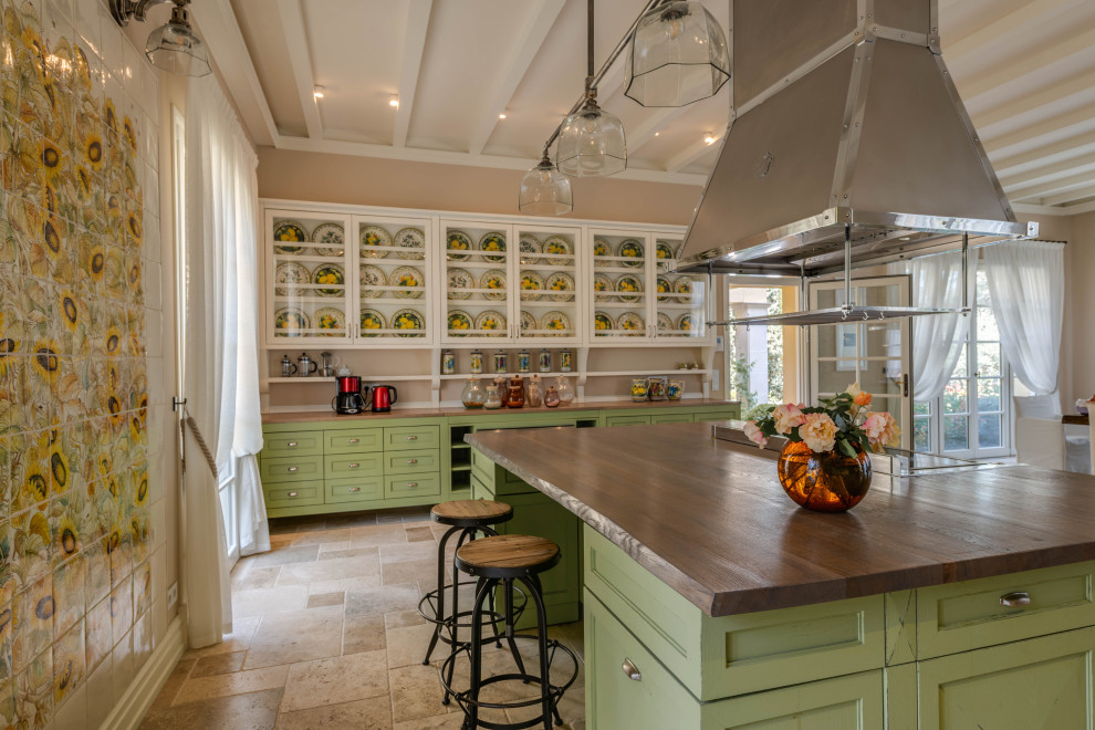 Design ideas for an expansive mediterranean single-wall eat-in kitchen in Other with recessed-panel cabinets, green cabinets, wood benchtops, stainless steel appliances, limestone floors, with island, beige floor and brown benchtop.