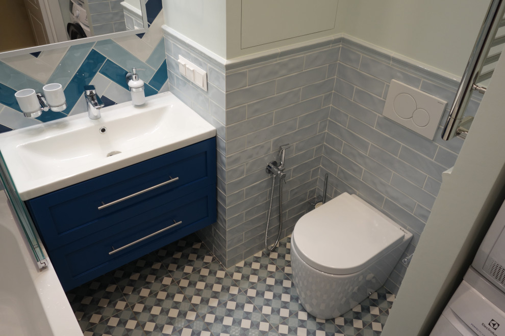 Cette image montre une salle de bain principale et grise et blanche marine de taille moyenne avec un placard avec porte à panneau surélevé, des portes de placard bleues, une baignoire encastrée, WC suspendus, un carrelage bleu, des carreaux de céramique, un mur bleu, un sol en carrelage de porcelaine, un lavabo posé, un plan de toilette en surface solide, un sol bleu, un plan de toilette blanc, buanderie, meuble simple vasque, meuble-lavabo suspendu et un plafond décaissé.