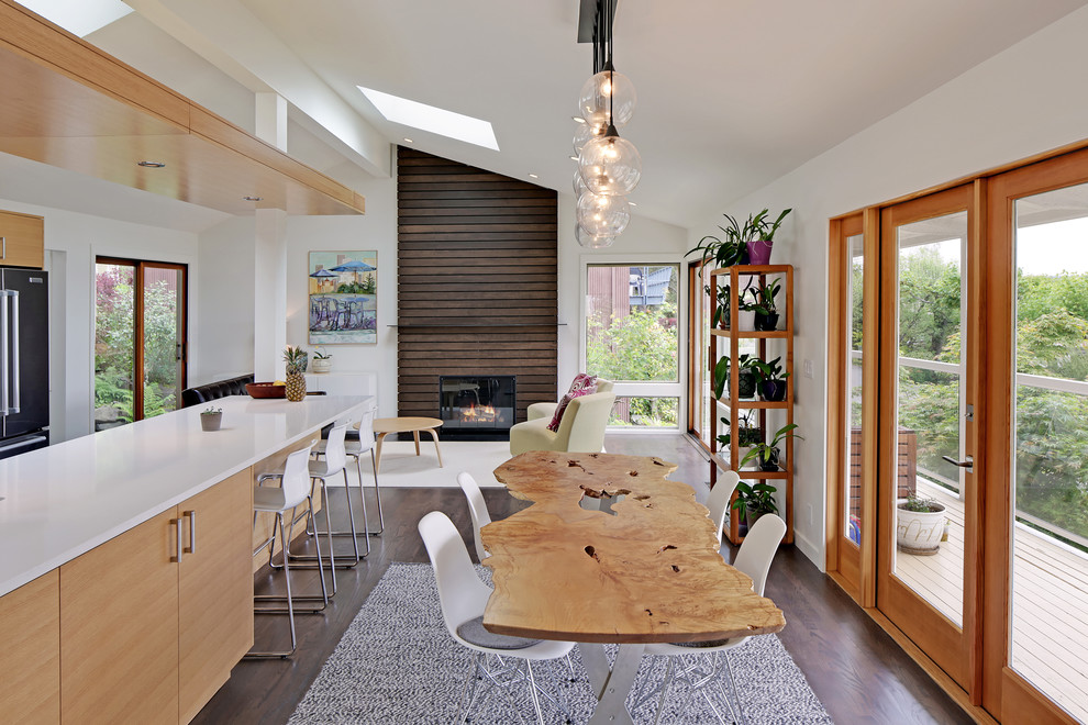 This is an example of a contemporary open plan dining in Seattle with white walls, dark hardwood floors, a standard fireplace and a wood fireplace surround.