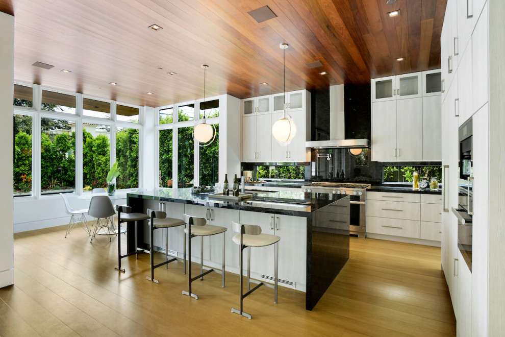 Inspiration for a contemporary kitchen in Los Angeles with an undermount sink, flat-panel cabinets, beige cabinets, black splashback, stainless steel appliances, light hardwood floors, with island, beige floor and black benchtop.