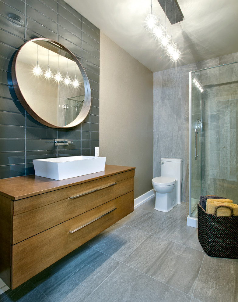 Mid-sized contemporary bathroom in Montreal with a vessel sink, flat-panel cabinets, medium wood cabinets, a corner shower, a one-piece toilet, gray tile, wood benchtops, porcelain tile, porcelain floors and brown benchtops.