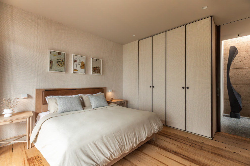 Photo of a modern bedroom in Hobart with beige walls, medium hardwood floors, brown floor and wallpaper.