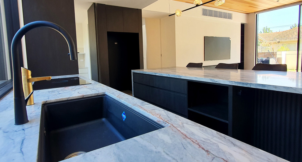 Photo of a mid-sized contemporary kitchen pantry in Melbourne with a single-bowl sink, black cabinets, marble benchtops, black appliances, ceramic floors, with island, grey floor and beige benchtop.