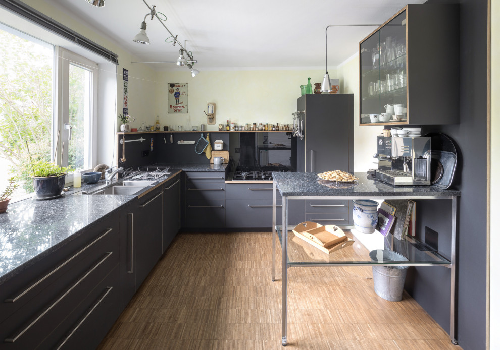 Geschlossene, Mittelgroße Industrial Küche in L-Form mit Doppelwaschbecken, grauen Schränken, Granit-Arbeitsplatte und schwarzen Elektrogeräten in Stuttgart