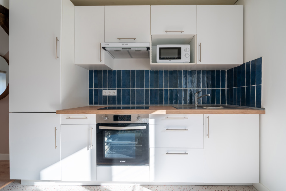 Idéer för mellanstora funkis linjära beige kök med öppen planlösning, med en undermonterad diskho, vita skåp, träbänkskiva, blått stänkskydd, stänkskydd i keramik, integrerade vitvaror, linoleumgolv och flerfärgat golv