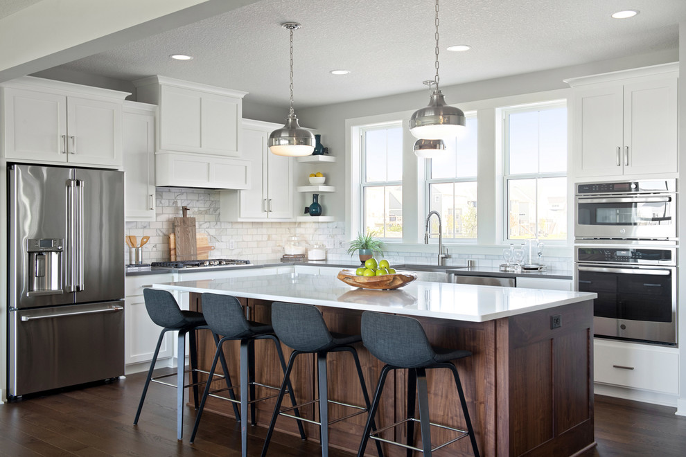 Inspiration for an expansive transitional l-shaped open plan kitchen in Minneapolis with a farmhouse sink, shaker cabinets, white cabinets, granite benchtops, subway tile splashback, stainless steel appliances, with island, white benchtop, white splashback, dark hardwood floors and brown floor.