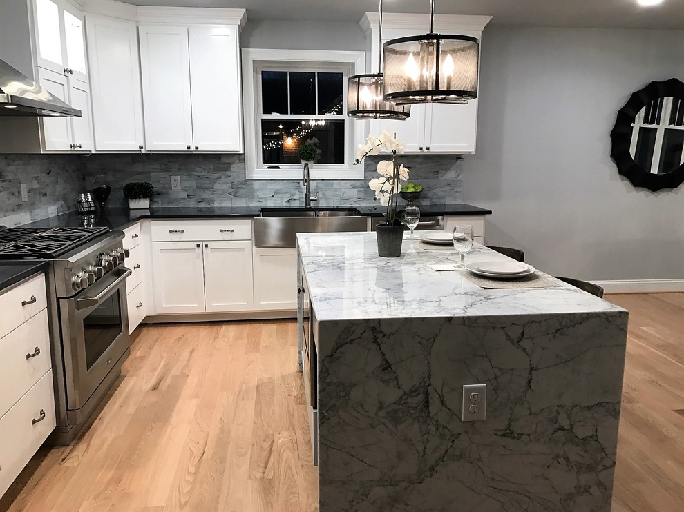 Mid-sized contemporary l-shaped eat-in kitchen in Richmond with a farmhouse sink, shaker cabinets, white cabinets, marble benchtops, multi-coloured splashback, porcelain splashback, stainless steel appliances, light hardwood floors, with island and beige floor.
