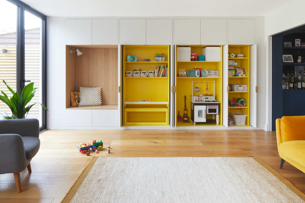 На фото: большая открытая гостиная комната в современном стиле с с книжными шкафами и полками, желтыми стенами, паркетным полом среднего тона, панелями на части стены и акцентной стеной без камина с