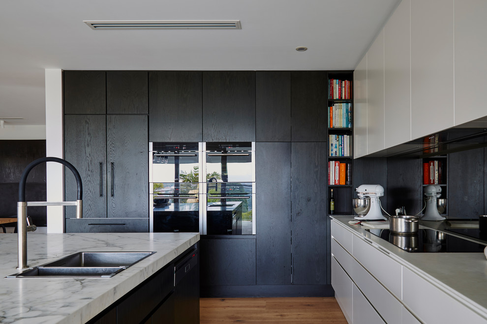 Design ideas for a contemporary l-shaped kitchen in Sydney with a drop-in sink, flat-panel cabinets, black cabinets, mirror splashback, black appliances, medium hardwood floors and with island.