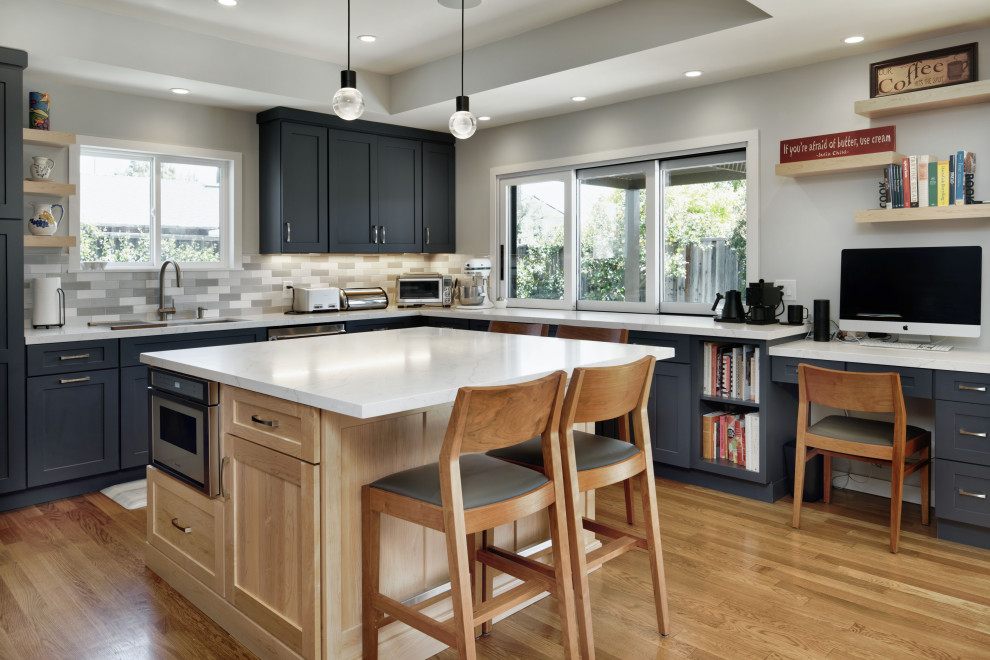 Photo of a mid-sized transitional u-shaped eat-in kitchen in San Francisco with an undermount sink, shaker cabinets, subway tile splashback, stainless steel appliances, medium hardwood floors, with island, white benchtop, recessed, blue cabinets, grey splashback, solid surface benchtops and brown floor.