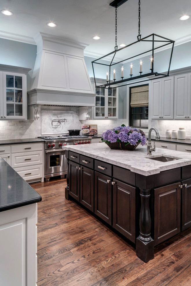 Design ideas for a traditional u-shaped kitchen in Dallas with an undermount sink, raised-panel cabinets, white cabinets, white splashback, stainless steel appliances, dark hardwood floors and with island.