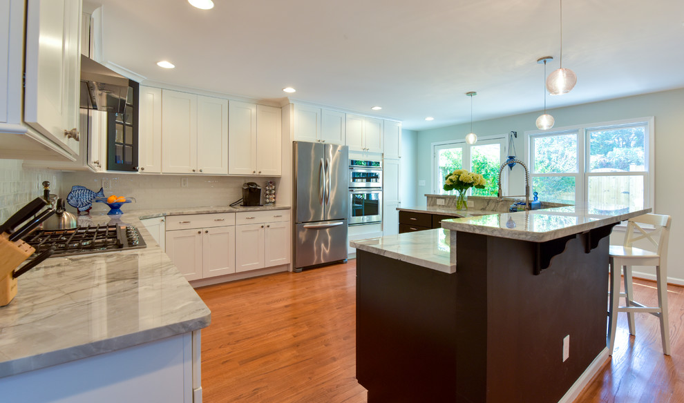 Photo of a large transitional l-shaped eat-in kitchen in DC Metro with shaker cabinets, white cabinets, marble benchtops, white splashback, stainless steel appliances, medium hardwood floors, with island and brown floor.