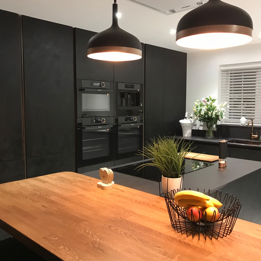 Design ideas for a mid-sized contemporary eat-in kitchen in Cambridgeshire with an integrated sink, flat-panel cabinets, black cabinets, quartz benchtops, black appliances, porcelain floors, with island, white floor and black benchtop.