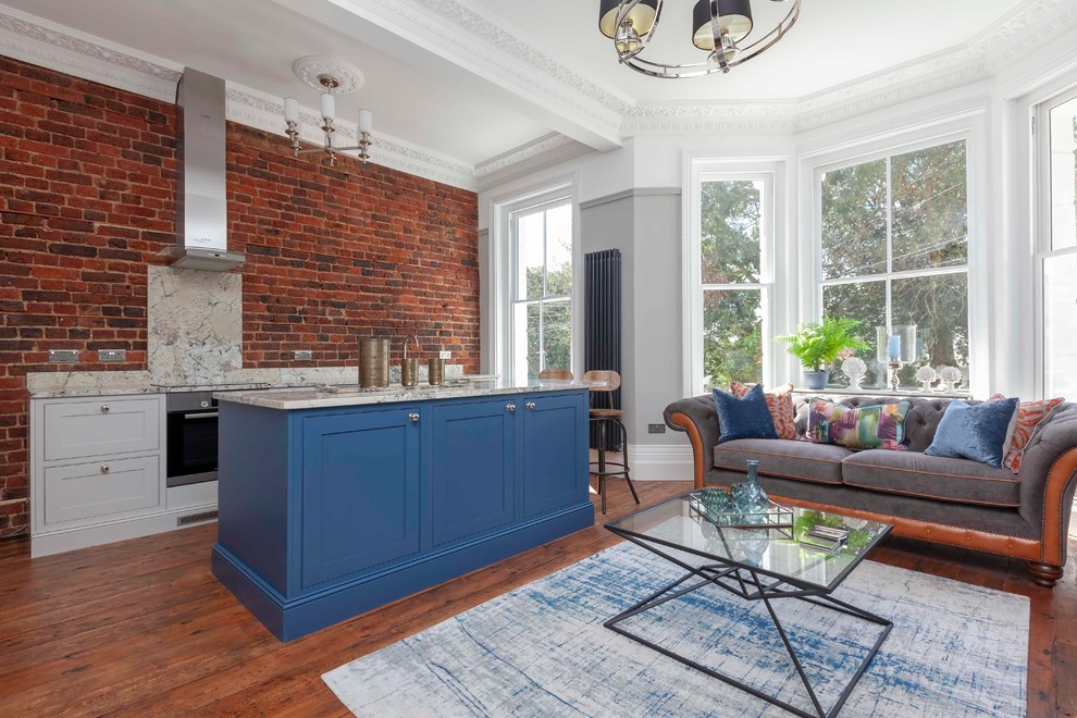 Photo of a small eclectic single-wall open plan kitchen in Sussex with shaker cabinets, blue cabinets, with island, granite benchtops, stainless steel appliances, medium hardwood floors, red floor and beige benchtop.