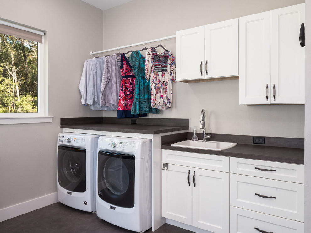 This is an example of a mid-sized transitional single-wall utility room in Miami with a drop-in sink, shaker cabinets, white cabinets, solid surface benchtops, white walls, dark hardwood floors, a side-by-side washer and dryer, brown floor and black benchtop.