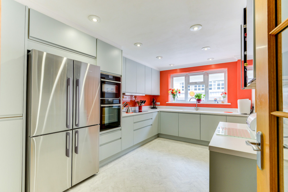 Medium sized nautical grey and white l-shaped enclosed kitchen in Sussex with a built-in sink, flat-panel cabinets, green cabinets, composite countertops, orange splashback, glass sheet splashback, black appliances, lino flooring, a breakfast bar, white floors, white worktops and feature lighting.