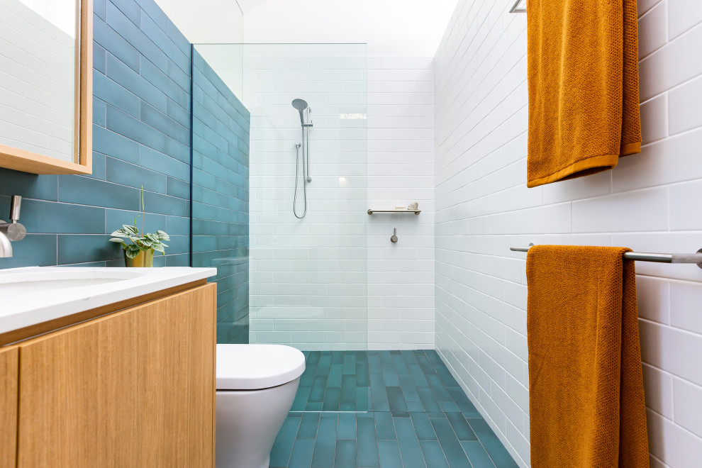 Photo of a small contemporary ensuite bathroom in Canberra - Queanbeyan with brown cabinets, a one-piece toilet, cement tiles, white walls, cement flooring, engineered stone worktops, blue floors, a wall niche, a single sink, a floating vanity unit, a vaulted ceiling and flat-panel cabinets.