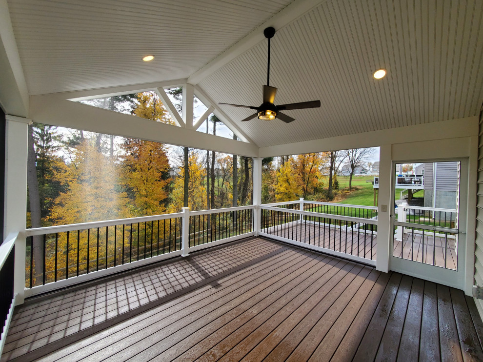 Cette image montre un grand porche d'entrée de maison arrière traditionnel avec une moustiquaire, une terrasse en bois, une extension de toiture et un garde-corps en matériaux mixtes.