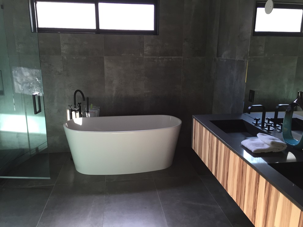 Large modern master bathroom in Los Angeles with flat-panel cabinets, light wood cabinets, a freestanding tub, an alcove shower, gray tile, cement tile, grey walls, cement tiles, an undermount sink, solid surface benchtops, grey floor and a hinged shower door.