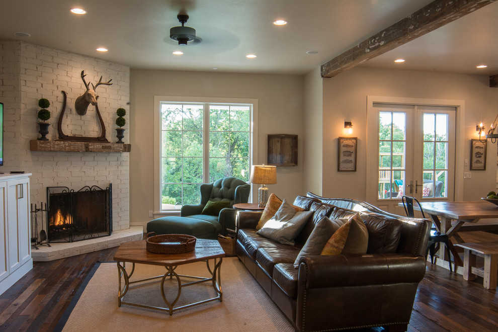 Photo of a mid-sized country open concept family room in Oklahoma City with white walls, dark hardwood floors, a corner fireplace, a brick fireplace surround, a freestanding tv and brown floor.