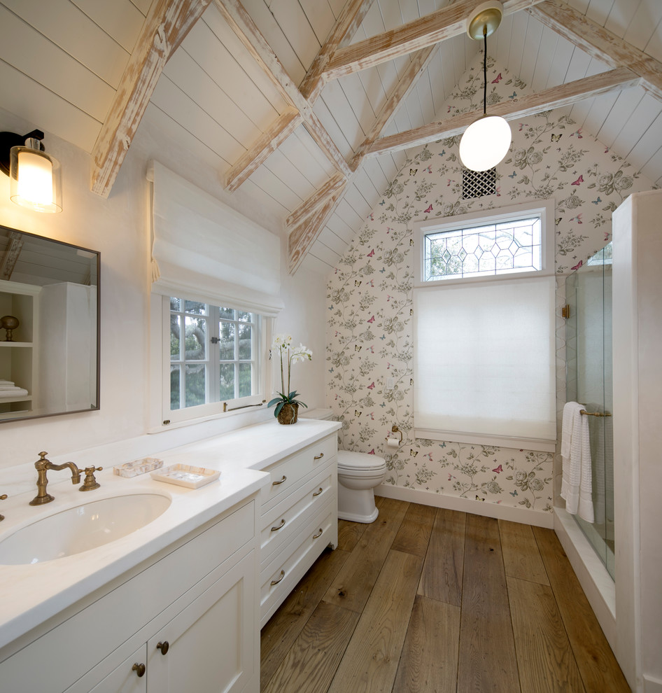 Inspiration for a mid-sized traditional bathroom in Santa Barbara with shaker cabinets, white cabinets, a two-piece toilet, white walls, light hardwood floors, an undermount sink, marble benchtops, a hinged shower door and white benchtops.