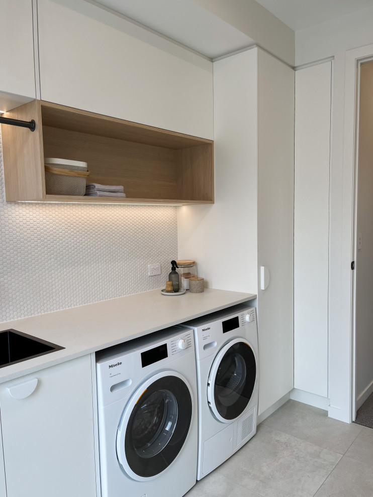 Inspiration for a mid-sized contemporary single-wall dedicated laundry room in Hamilton with an undermount sink, flat-panel cabinets, white cabinets, laminate benchtops, white splashback, mosaic tile splashback, white walls, porcelain floors, a side-by-side washer and dryer, grey floor and white benchtop.