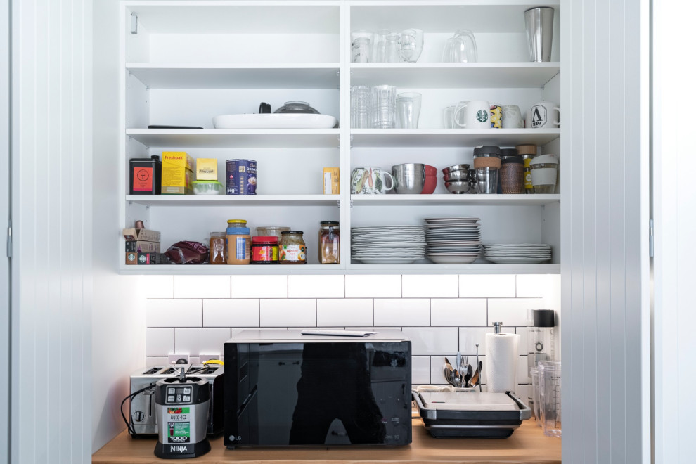 This is an example of a country kitchen with a single-bowl sink, shaker cabinets, white cabinets, quartz benchtops, white splashback, ceramic splashback, black appliances, light hardwood floors, with island, beige floor and white benchtop.