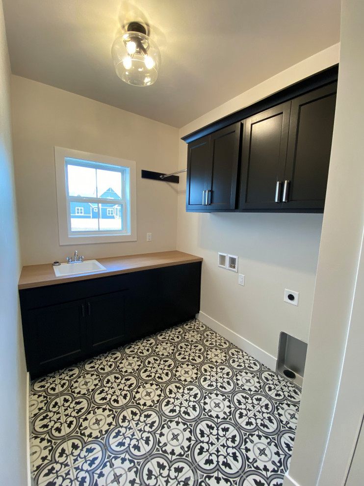 This is an example of a mid-sized country l-shaped dedicated laundry room in Other with an utility sink, shaker cabinets, black cabinets, laminate benchtops, ceramic floors, a side-by-side washer and dryer, black floor and brown benchtop.