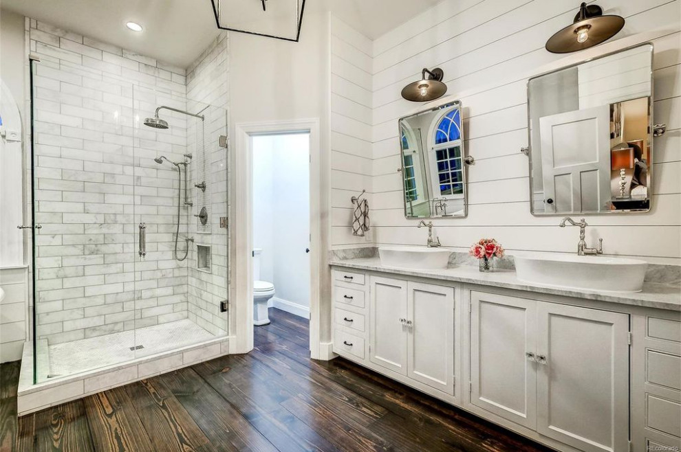 Mid-sized country master bathroom in Denver with beaded inset cabinets, white cabinets, a freestanding tub, a corner shower, a one-piece toilet, white tile, marble, white walls, dark hardwood floors, a vessel sink, marble benchtops, brown floor, a hinged shower door and grey benchtops.