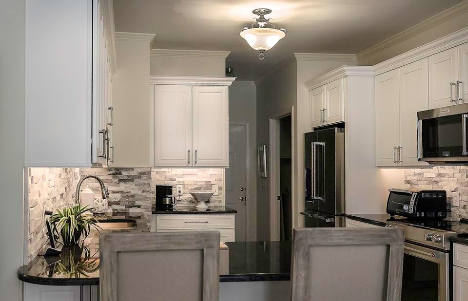 Transitional l-shaped kitchen photo with an undermount sink, recessed-panel cabinets, white cabinets, granite countertops, gray backsplash, stone tile backsplash, stainless steel appliances and a peninsula