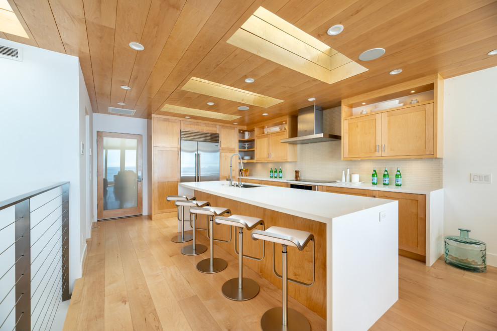 Design ideas for an expansive contemporary l-shaped kitchen in Los Angeles with a single-bowl sink, shaker cabinets, quartz benchtops, beige splashback, glass tile splashback, stainless steel appliances, with island, white benchtop, medium wood cabinets, medium hardwood floors and brown floor.