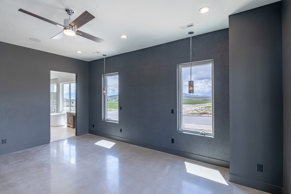 Large country master bedroom in Salt Lake City with black walls, concrete floors, a standard fireplace, a plaster fireplace surround and grey floor.